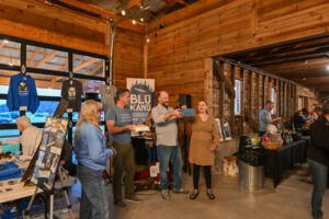 Group of people engaging at a community event in a rustic venue, showcasing local vendors and promoting the Spooner Area Chamber of Commerce's Food & Wine Tasting Benefit.