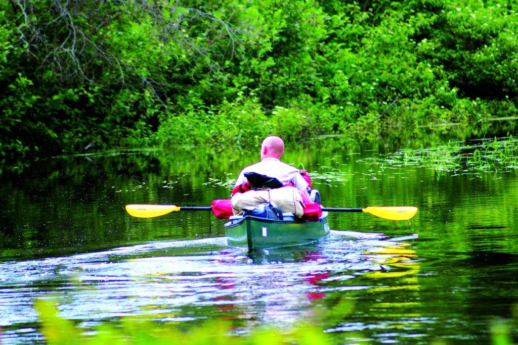 Person kayaking on a tranquil waterway surrounded by lush greenery in Spooner, Wisconsin, reflecting the region's scenic beauty and outdoor activities.