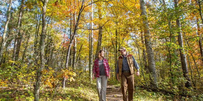 Couple walking along a scenic forest trail surrounded by vibrant autumn foliage in Spooner, Wisconsin, highlighting fall colors and outdoor activities.