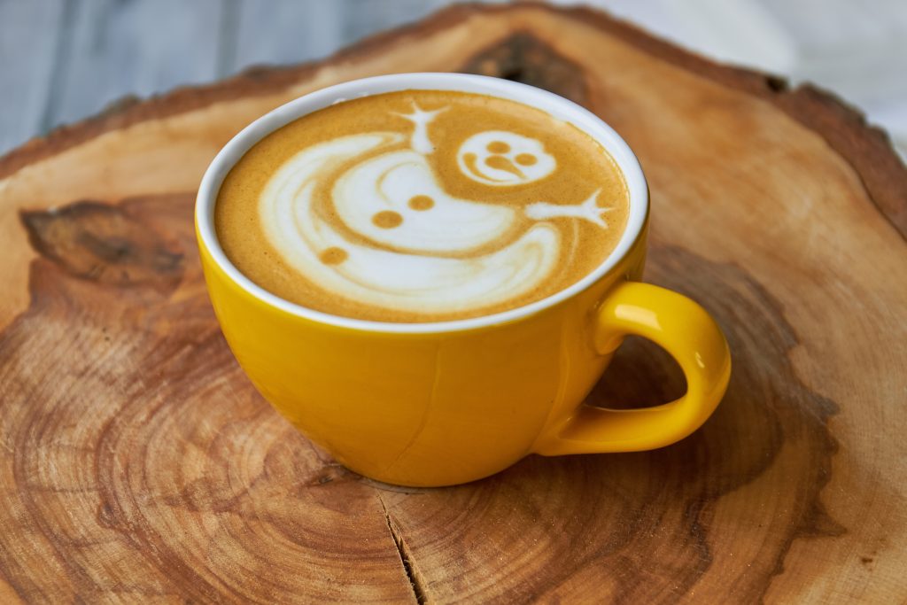 Snowman latte art in a yellow coffee cup on a wooden surface, representing cozy winter vibes in Spooner's coffee scene.
